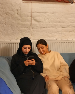 Zwei Mädchen sitzen auf einer Couch und reden miteinander.