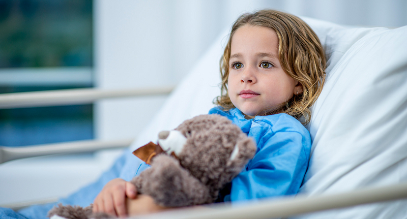 Kind im Krankenhausbett mit Teddybär