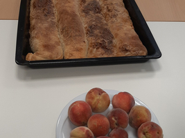 Ein Blech mit drei Strudeln und ein Teller mit Pfirsichen.
