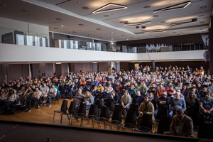 Ein Publikum sitzt in einem großen Saal während einer Veranstaltung.