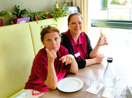 Zwei Frauen in roten Poloshirts lächeln und genießen ihr Essen am Tisch.