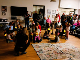 Kinder mit Laternen stehen in einem Gemeinschaftsraum vor einer größeren Gruppe von Menschen.