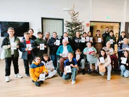 Eine Gruppe von Menschen hält Karten vor einem Weihnachtsbaum in einem Gemeinschaftsraum.