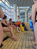 Eine Gruppe von Schwimmerinnen hört einem Trainer am Beckenrand zu.