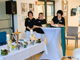 Drei Frauen in schwarzer Kleidung präsentieren eine festliche Tischdekoration.