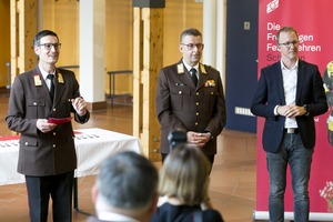 Drei Personen in Uniformen stehen bei einer Veranstaltung zusammen und reden.