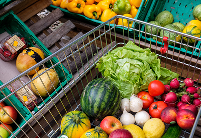 Ein mit Gemüse und Obst befüllter Einkaufswagen steht vor Regalen der Obstabteilung, Sozialmarkt, Nahrungsmittelspenden  