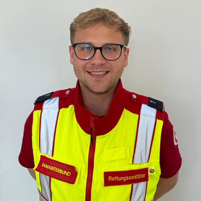 Ein Rettungssanitäter lächelt in einer gelben und roten Uniform.