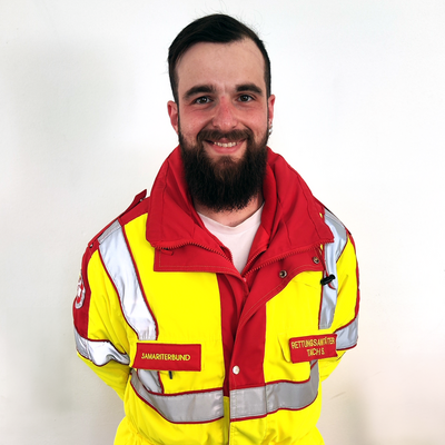 Ein lächelnder Mann in einem auffälligen gelben Rettungsdienst-Jacke.