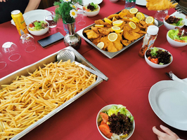 Ein Tisch mit verschiedenen Gerichten: Ausgiebige Portionen von Pommes frites in einer großen Schüssel, knusprige Hähnchenfilets, garniert mit Zitronenscheiben, und mehrere kleine Schüsseln mit gemischtem Salat.