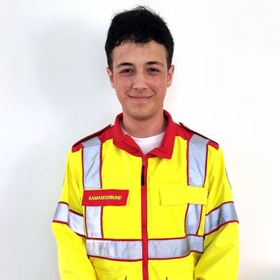 Junger Mann in reflektierender Sanitäterjacke mit einem freundlichen Lächeln.