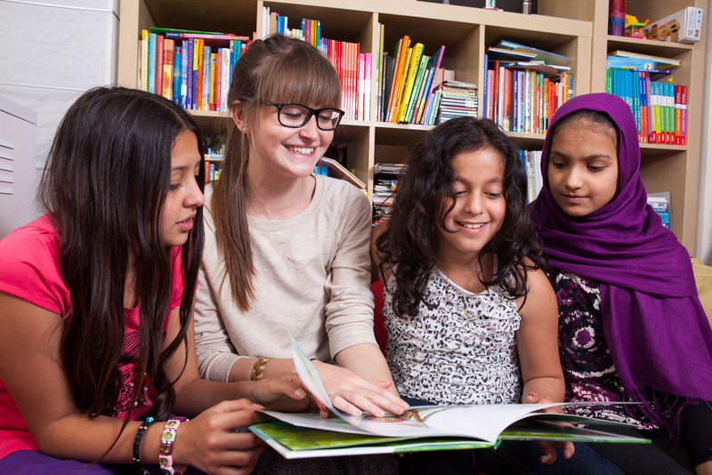 Vier Kinder sitzen zusammen vor einem Bücherregal und lesen ein Buch, LernLEO