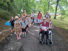 Gruppe aus Kindern und Senioren auf einem grünen Weg unter Bäumen.