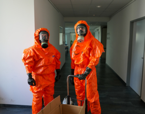 Zwei Personen im orangen Schutzanzug mit Atemschutzmaske