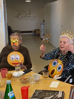 Zwei Senioren mit Emoji-Masken feiern gemeinsam an einem Tisch.