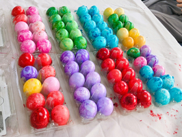 Bunte Ostereier in verschiedenen Farben liegen ordentlich auf einem Tisch. Die Eier sind in mehreren Reihen angeordnet, wobei jede Reihe eine andere Farbkombination zeigt, darunter Rot, Pink, Lila, Blau, Grün und Gelb. Einige Eier zeigen marmorierte Muster.
