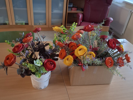 Zwei bunte Blumenarrangements in Töpfen auf einem Holztisch.