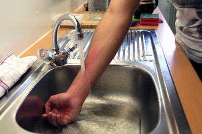 Eine Hand taucht in ein Waschbecken mit fließendem Wasser.
