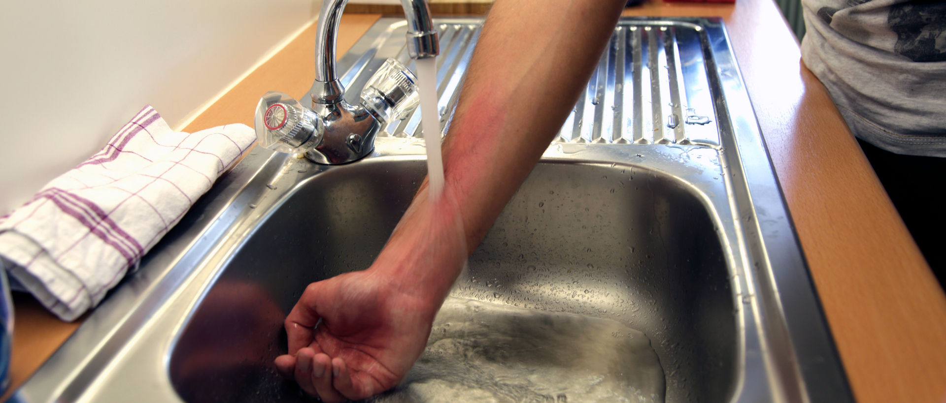 Eine Hand taucht in ein Waschbecken mit fließendem Wasser.