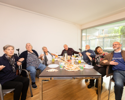 Rund um einen Tisch sitzen sieben Senior:innen und lachen miteinander.