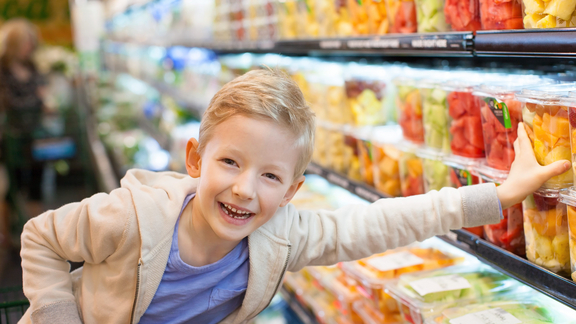 Kleiner Junge greift zu frischem Obst in Supermarkt-Regal