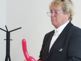 Ein Mann hält einen roten Luftballon in Form eines Hundes.