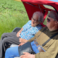 Zwei lächelnde Senioren sitzen gemeinsam in einem Fahrzeug im Freien.
