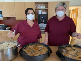 Zwei Frauen kochen in einer Küche, eine rührt Reis, die andere brät Lebensmittel.