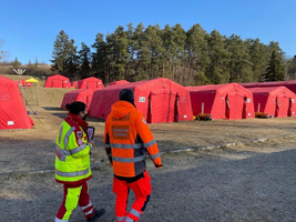 Zwei Rettungskräfte gehen an roten Zelten in einer Lichtung vorbei.