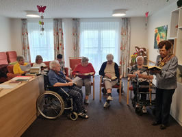 Ältere Frauen lesen in einer gemeinsamen Runde, eine Frau steht und liest vor.