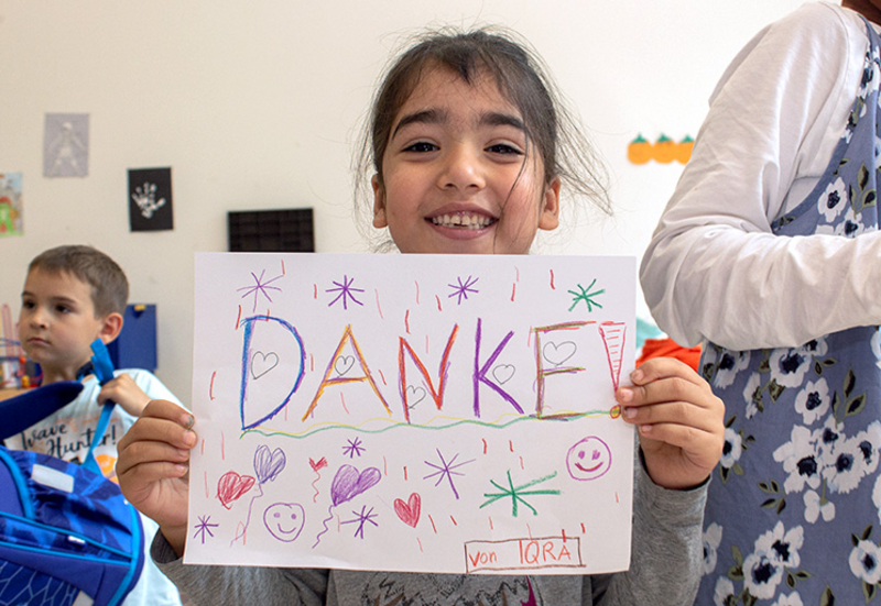 Ein junges Mädchen hält einen Zettel vor sich, auf dem DANKE steht, Familien in Not