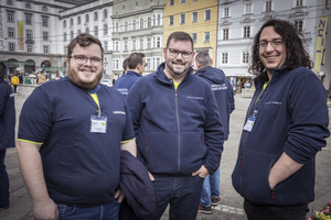 Drei Männer in Samaritershirts lächeln zusammen in einer Stadtumgebung.