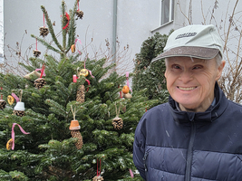 Lächelnder älterer Mann steht neben einem geschmückten Weihnachtsbaum.