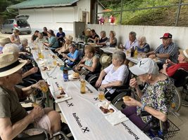 Ältere Menschen genießen ein gemeinsames Essen an einem langen Tisch im Freien.