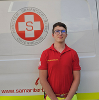 Ein Sanitäter in Uniform steht vor einem Rettungsauto des Samariterbundes.