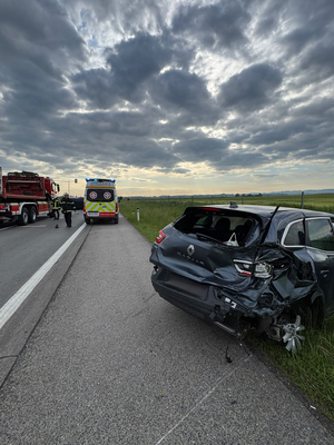 Unfallstelle mit beschädigtem Auto und Einsatzfahrzeugen auf der Straße.