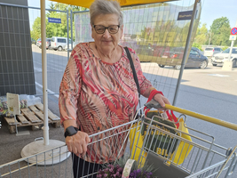 Eine ältere Frau mit einem Einkaufswagen, der mit Blumen gefüllt ist.