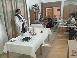 Ein Mann in liturgischer Kleidung spricht vor einer Gruppe älterer Menschen.