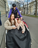 Drei Personen in einem Fahrradanhänger, lächelnd und in warmer Kleidung.