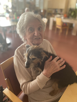 Eine ältere Frau hält einen Hund auf ihrem Schoß und lächelt.