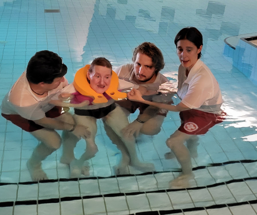 Vier Personen helfen einem Mann mit einem Schwimmring im Wasser.