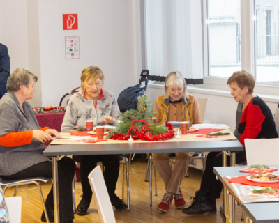 vier Senioren an einem Tisch, singen Lieder, weihnachtliche Dekoration