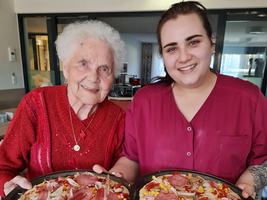 Zwei Frauen lächeln und halten frische Pizzen mit verschiedenen Belägen.