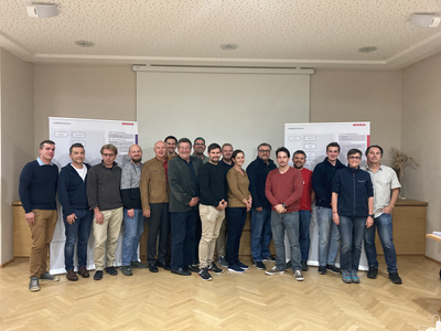 Gruppe von 15 Personen steht vor Präsentationswänden in einem Raum.