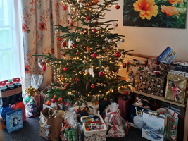 Weihnachtsbaum mit Lichtern und vielen Geschenken darunter in einem Wohnzimmer.