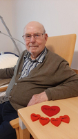 Älterer Mann sitzt neben roten Herzen mit den Namen seiner Familie.