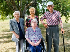 Vier ältere Menschen stehen unter einem Baum, ein Mann hält einen Gehstock.
