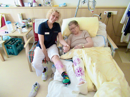 Eine Pflegekraft lächelt und hält die Hand einer älteren Patientin im Krankenhaus.