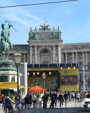 Bühne auf Heldenplatz in Wien, vor Hofburg aufgebaut, einige Menschen schon vor Bühne, Banner und Plakate, blauer Himmel 