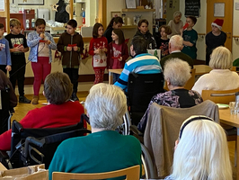 Kinder führen ein Weihnachtsprogramm für Senioren in einem Gemeinschaftsraum auf.